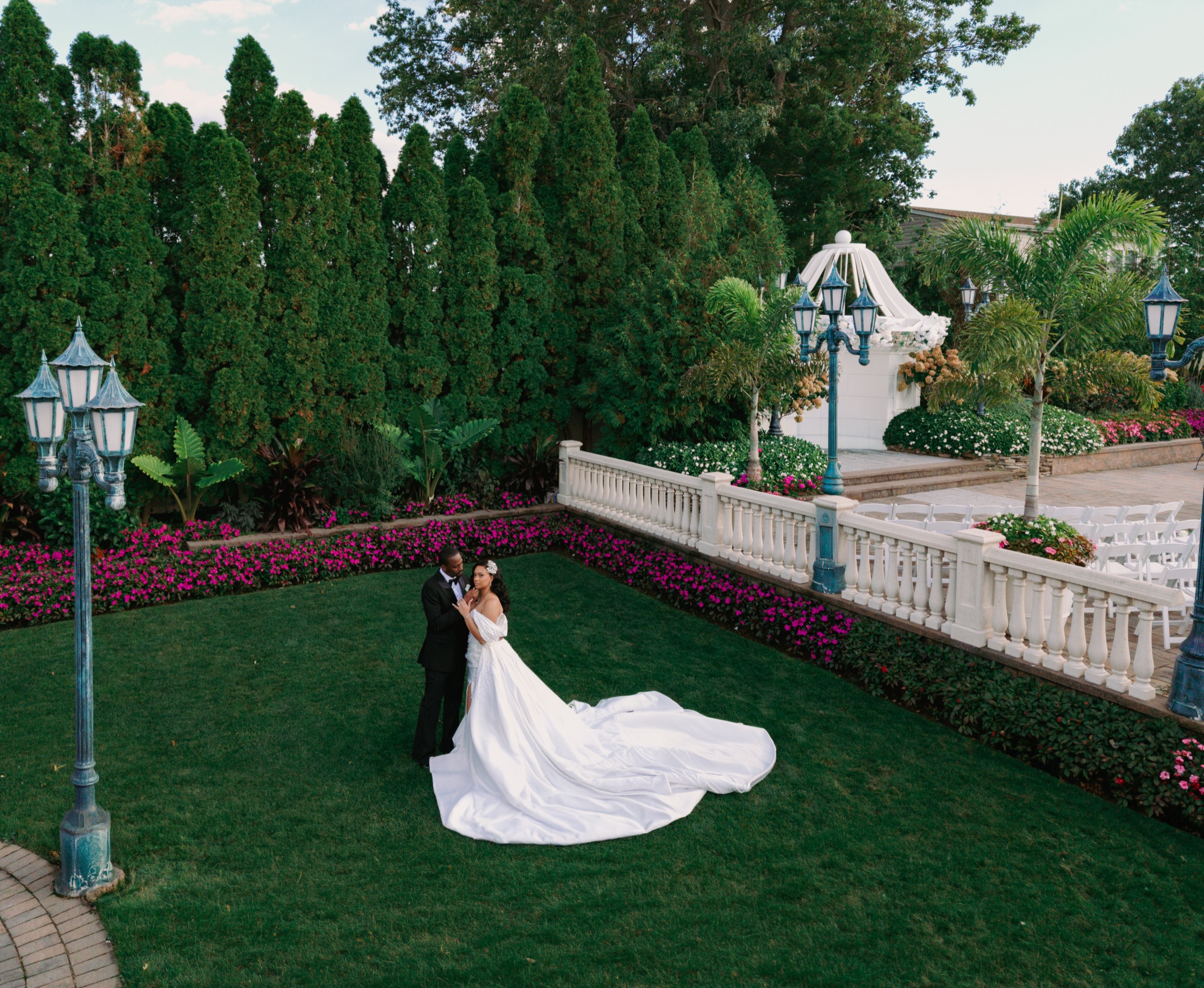 Bride and groom on a garden lawn, her long train spread across the grass